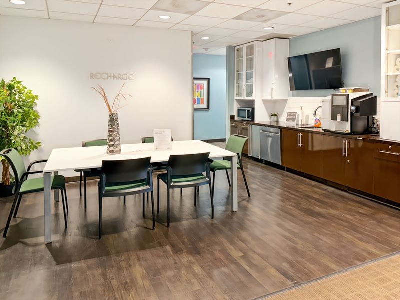 A modern office breakroom featuring built-in cabinetry, integrated dishwasher, sink, and a dining area for staff.