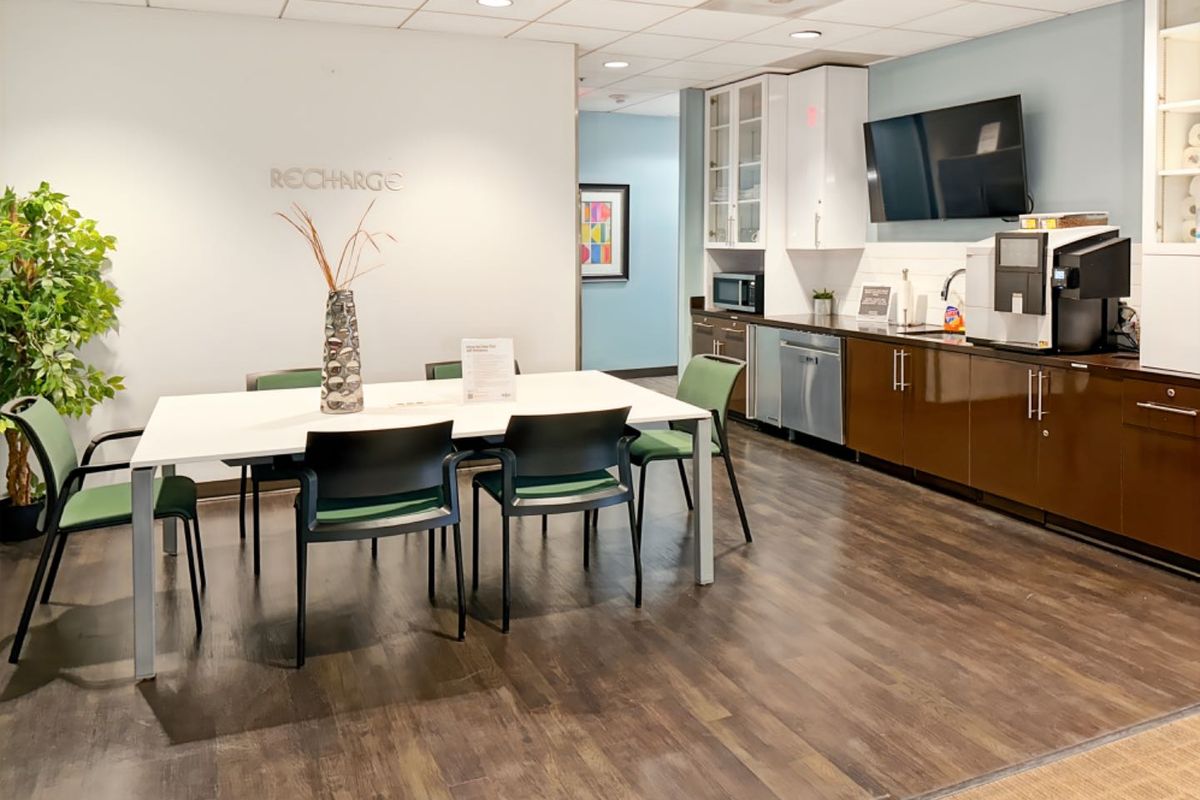 A modern office breakroom featuring built-in cabinetry, integrated dishwasher, sink, and a dining area for staff.