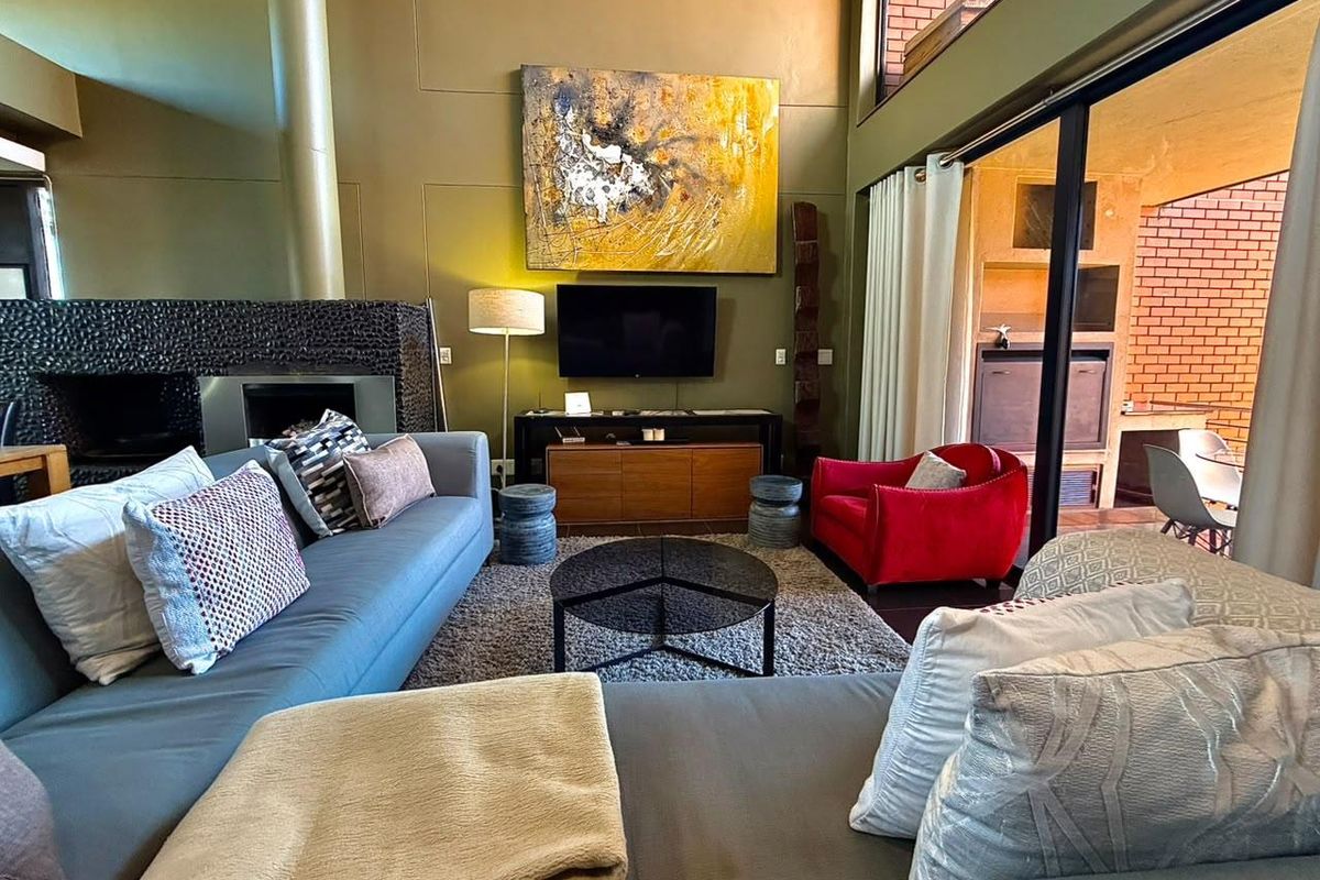 Spacious living room featuring a double-volume ceiling, a built-in fireplace with textured surround, and large sliding doors opening to an outdoor patio area.