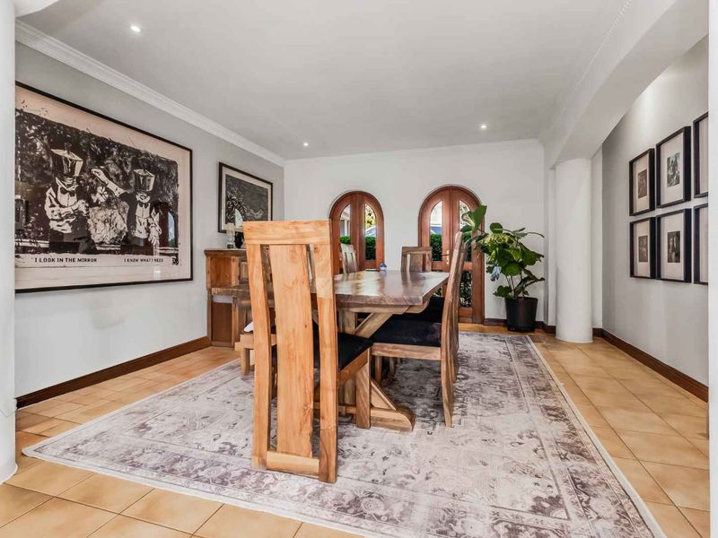 A well-maintained dining room featuring ceramic tile flooring, recessed lighting, and distinctive arched wooden doors leading to the exterior.