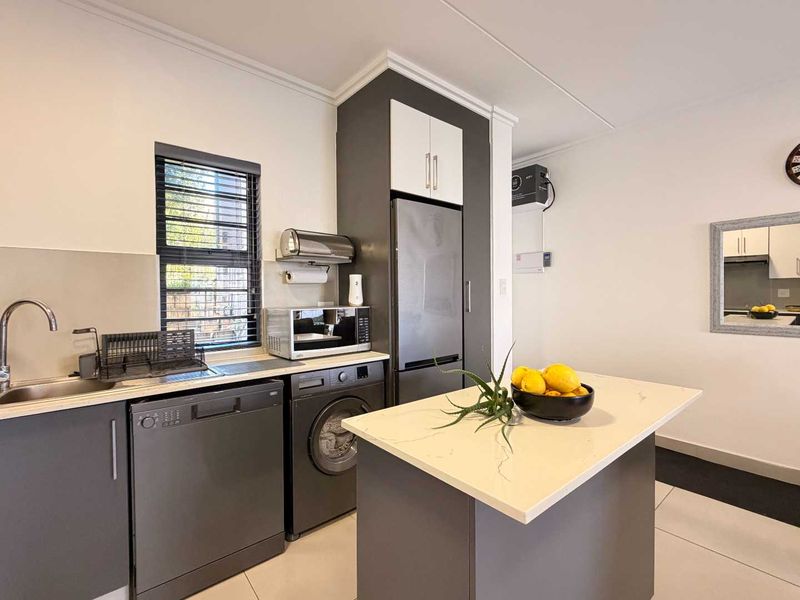 Modern kitchen featuring dark grey cabinetry, stone countertops, a central island, and integrated appliance spaces, finished with clean tiled flooring and neutral walls.