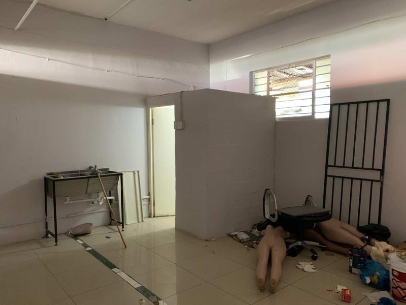 A functional utility space featuring tiled flooring, a stainless steel sink, and a security gate, suitable for storage or back-of-house operations.