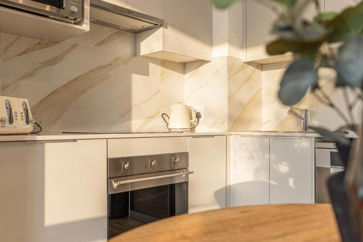 Modern kitchen featuring sleek white cabinetry, marble-look splashback, built-in oven, microwave, and extractor fan, offering a clean and contemporary aesthetic.