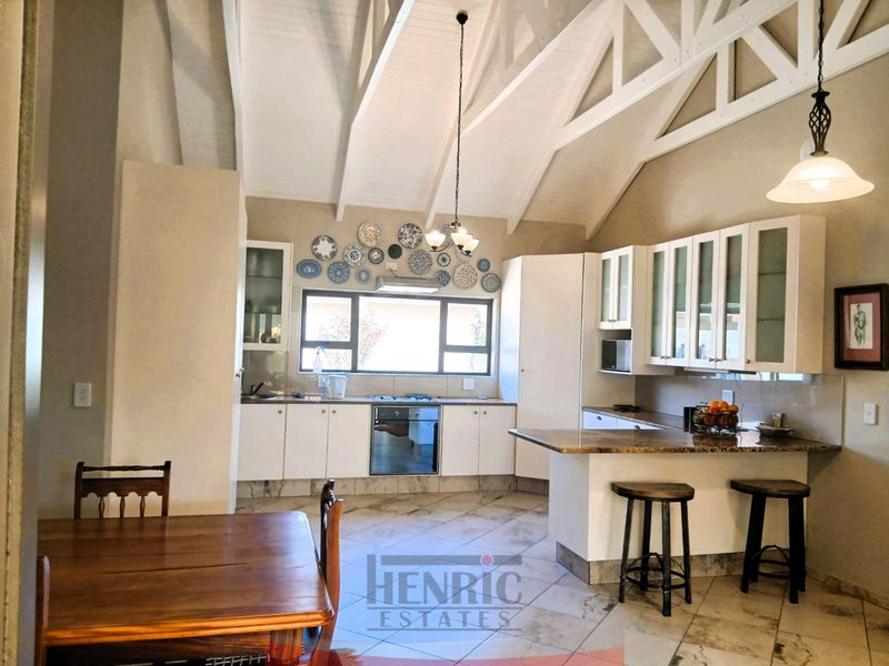 Spacious open-plan kitchen featuring vaulted ceilings with exposed trusses, granite countertops, built-in oven, gas hob, and ample cabinetry, seamlessly flowing into the dining area.