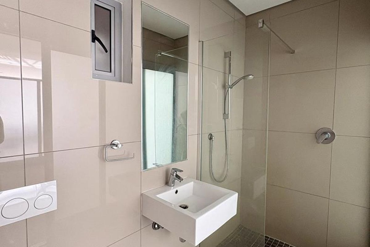 Modern bathroom featuring a wall-mounted basin, glass-enclosed walk-in shower with mosaic floor tiles, and neutral wall tiling.