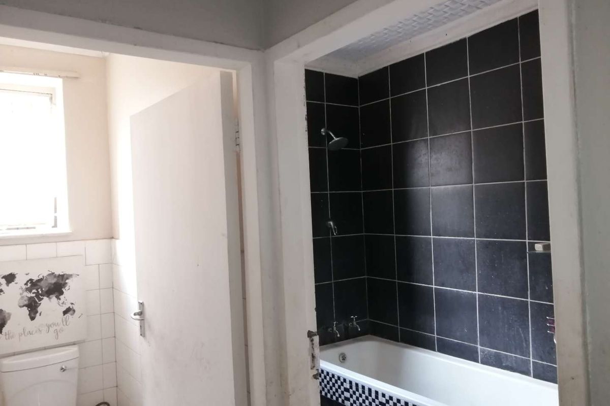 A functional bathroom featuring a bathtub with shower mixer, black wall tiling, and a separate toilet area with white wall tiles.