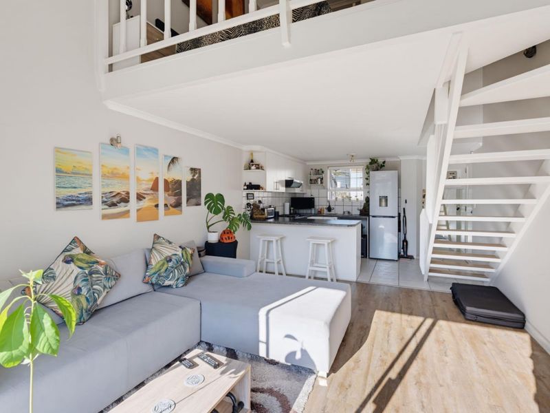 Open-plan living area featuring a compact kitchen, laminate flooring, and a staircase leading to a mezzanine level.