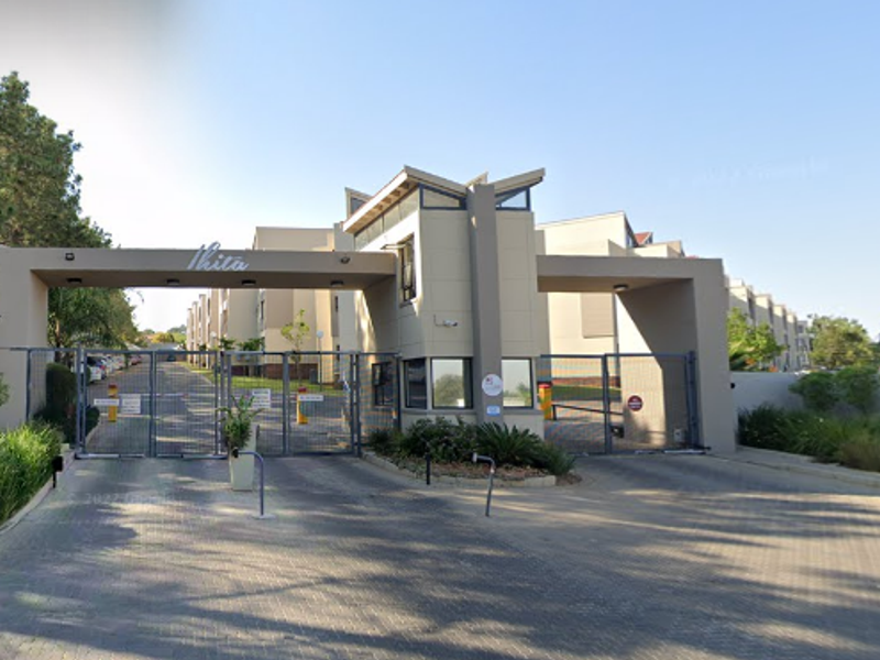 The main entrance to the apartment complex featuring a secure gated access point, guard house, and paved driveway.