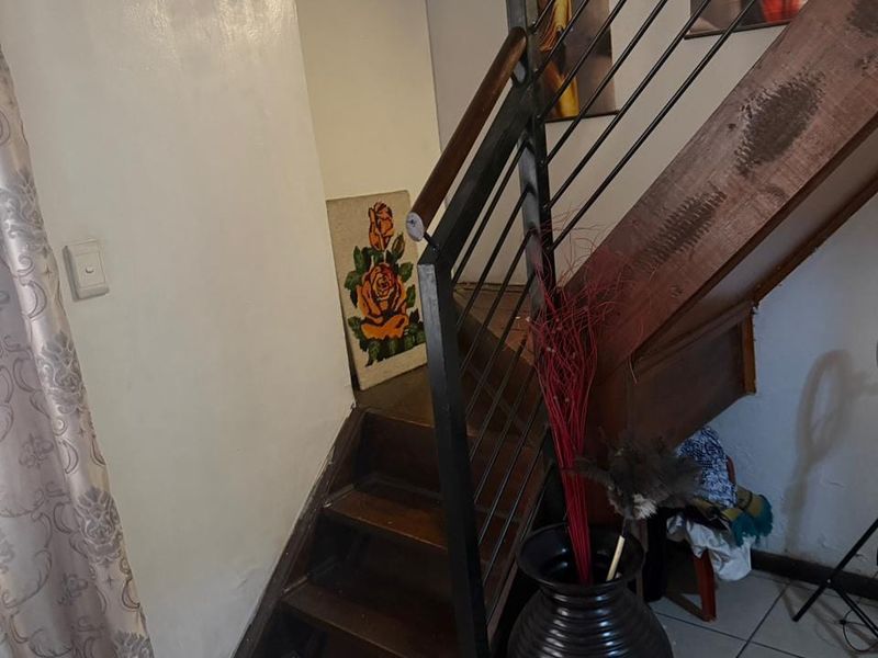 A hallway featuring a wooden staircase with a metal balustrade and tiled flooring, showing signs of wear and tear.