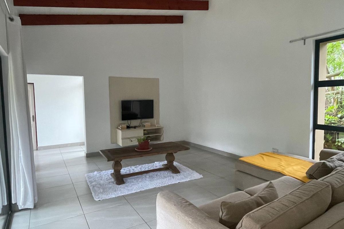 Spacious living room featuring high ceilings with exposed timber beams, large format floor tiles, and a built-in media console.