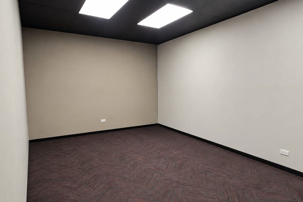 A clean, empty office space featuring dark carpet flooring, neutral walls, and recessed ceiling lighting, ready for professional use.