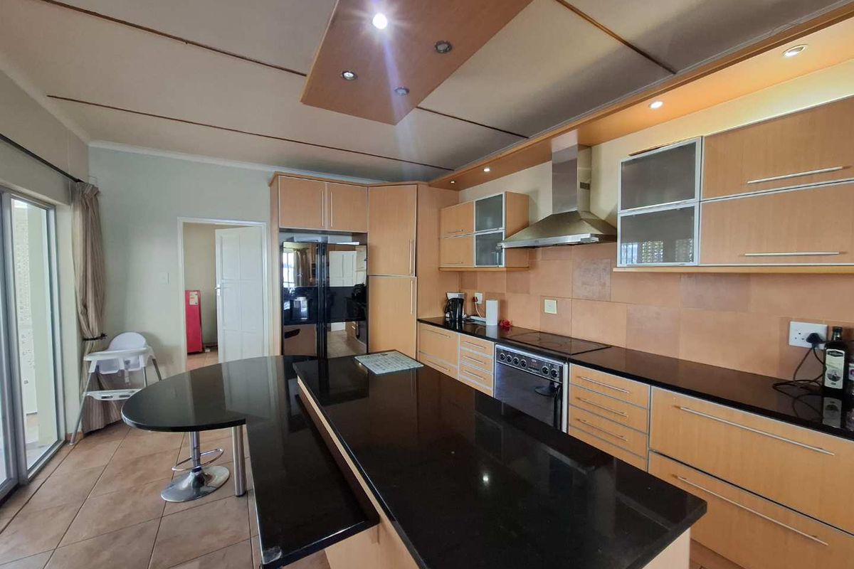 Modern kitchen featuring light wood cabinetry, black granite countertops, a central island with breakfast bar, and integrated stainless steel appliances.