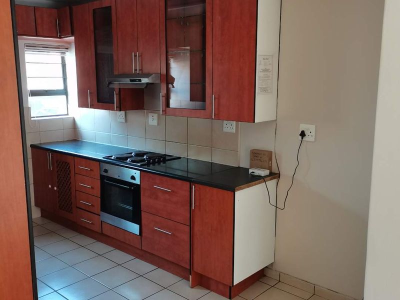 A functional kitchen featuring wood-tone cabinetry, black countertops, built-in oven, gas hob, and tiled flooring, offering a practical layout for daily use.