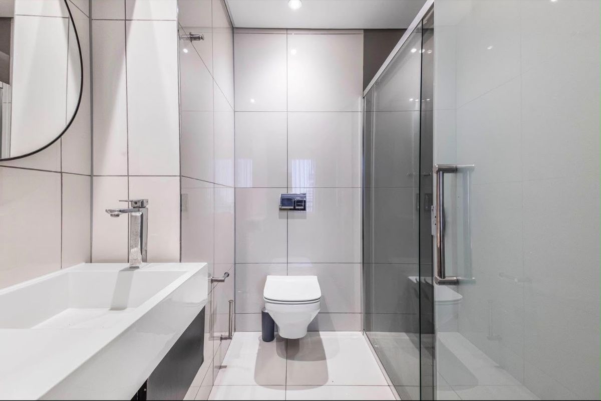 Modern bathroom featuring a wall-mounted toilet, glass shower enclosure, and a sleek vanity basin with contemporary chrome fixtures and neutral wall tiling.