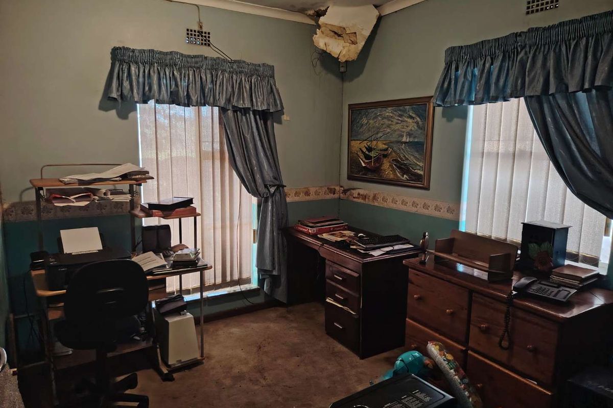 A bedroom or office space featuring dual windows, requiring significant ceiling repairs and cosmetic updates to the walls and flooring.