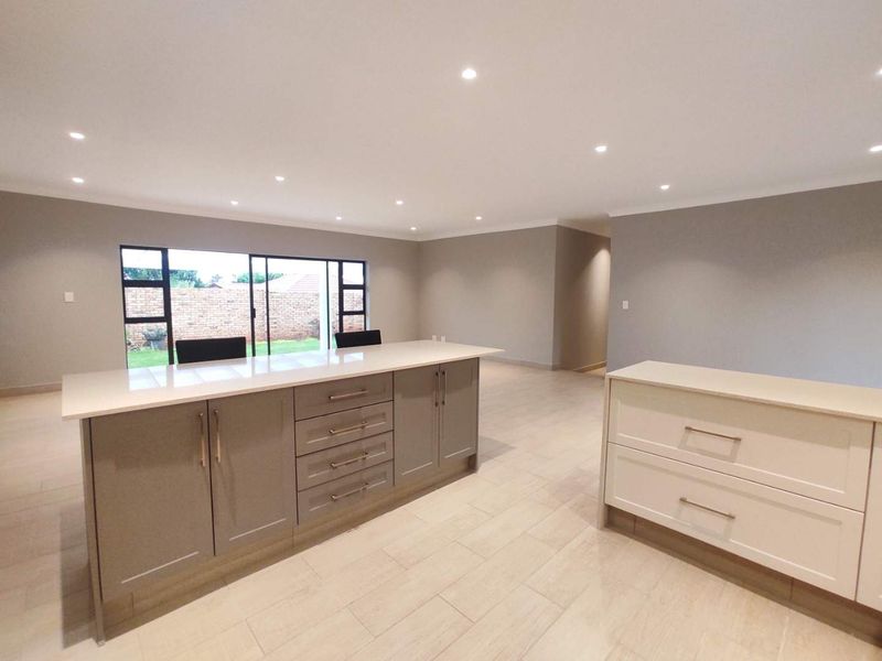 Spacious open-plan living area featuring a modern kitchen island, neutral tiled flooring, recessed lighting, and large sliding doors leading to the rear garden.
