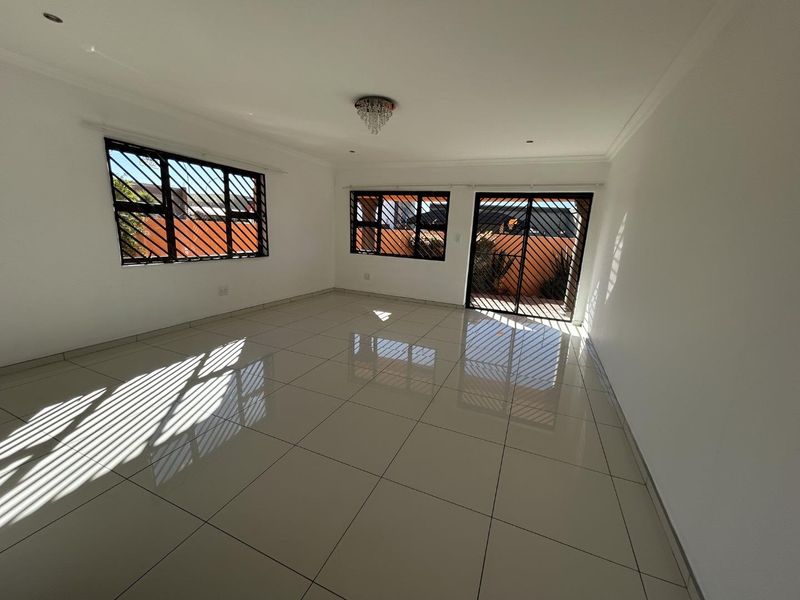 A bright, empty living room featuring polished porcelain floor tiles, security bars on windows, and a sliding door leading to the exterior.