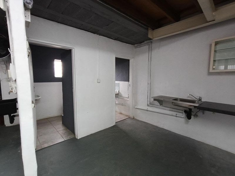 A functional utility space featuring a stainless steel sink, exposed plumbing, and direct access to adjacent washroom facilities.