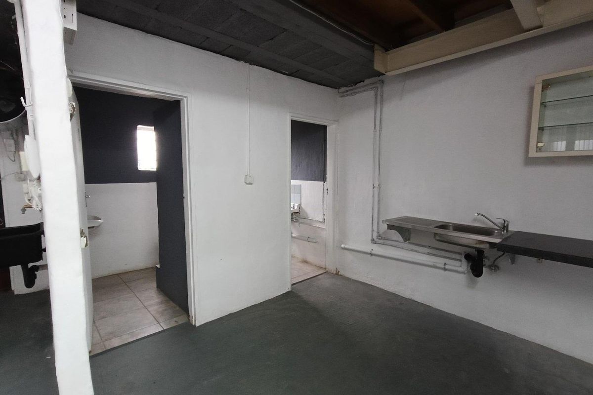 A functional utility space featuring a stainless steel sink, exposed plumbing, and direct access to adjacent washroom facilities.