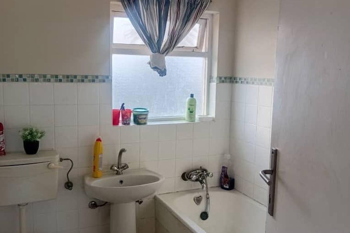 A functional bathroom featuring a pedestal basin, standard bathtub with shower mixer, and tiled walls with a decorative mosaic border.