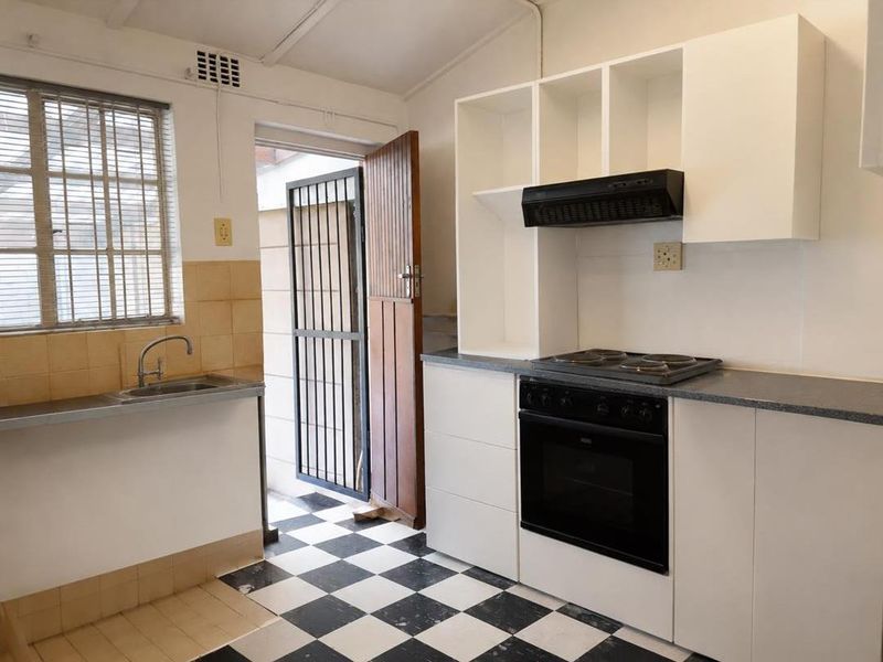 A functional kitchen featuring white cabinetry, built-in oven and hob, extractor fan, stainless steel sink, and a classic black and white checkered tiled floor.