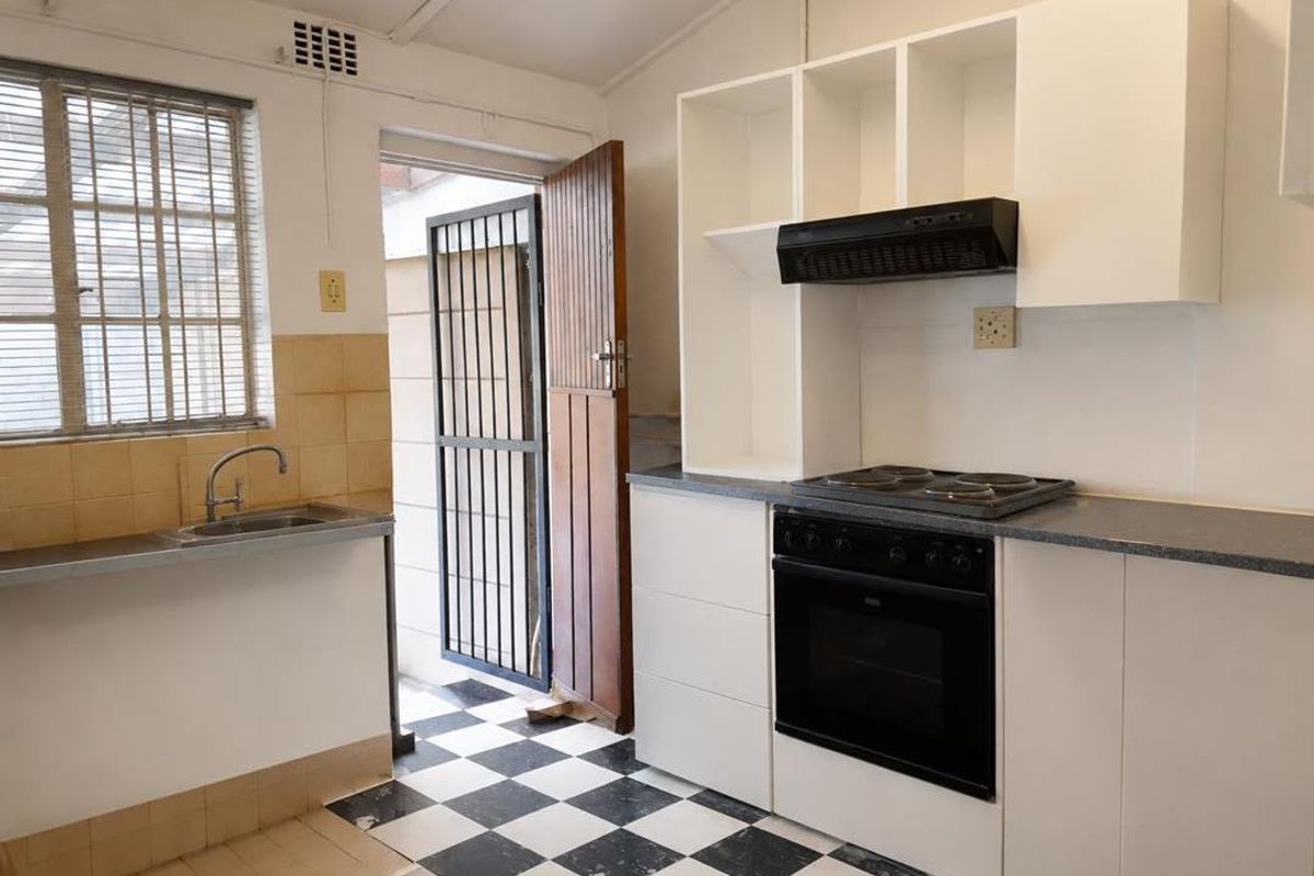 A functional kitchen featuring white cabinetry, built-in oven and hob, extractor fan, stainless steel sink, and a classic black and white checkered tiled floor.