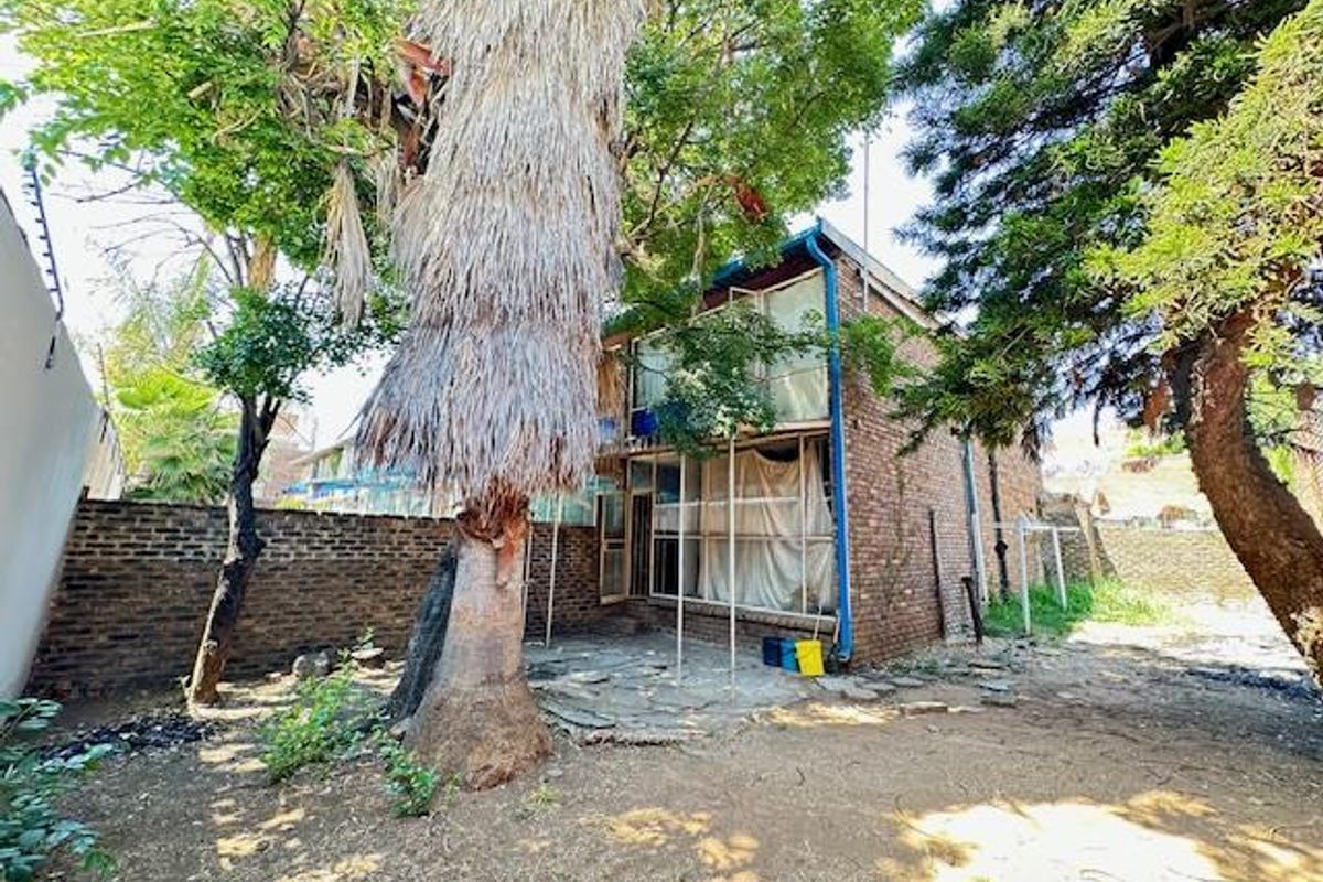 Rear view of the apartment building featuring a brick facade, paved patio area, and established garden space requiring maintenance.