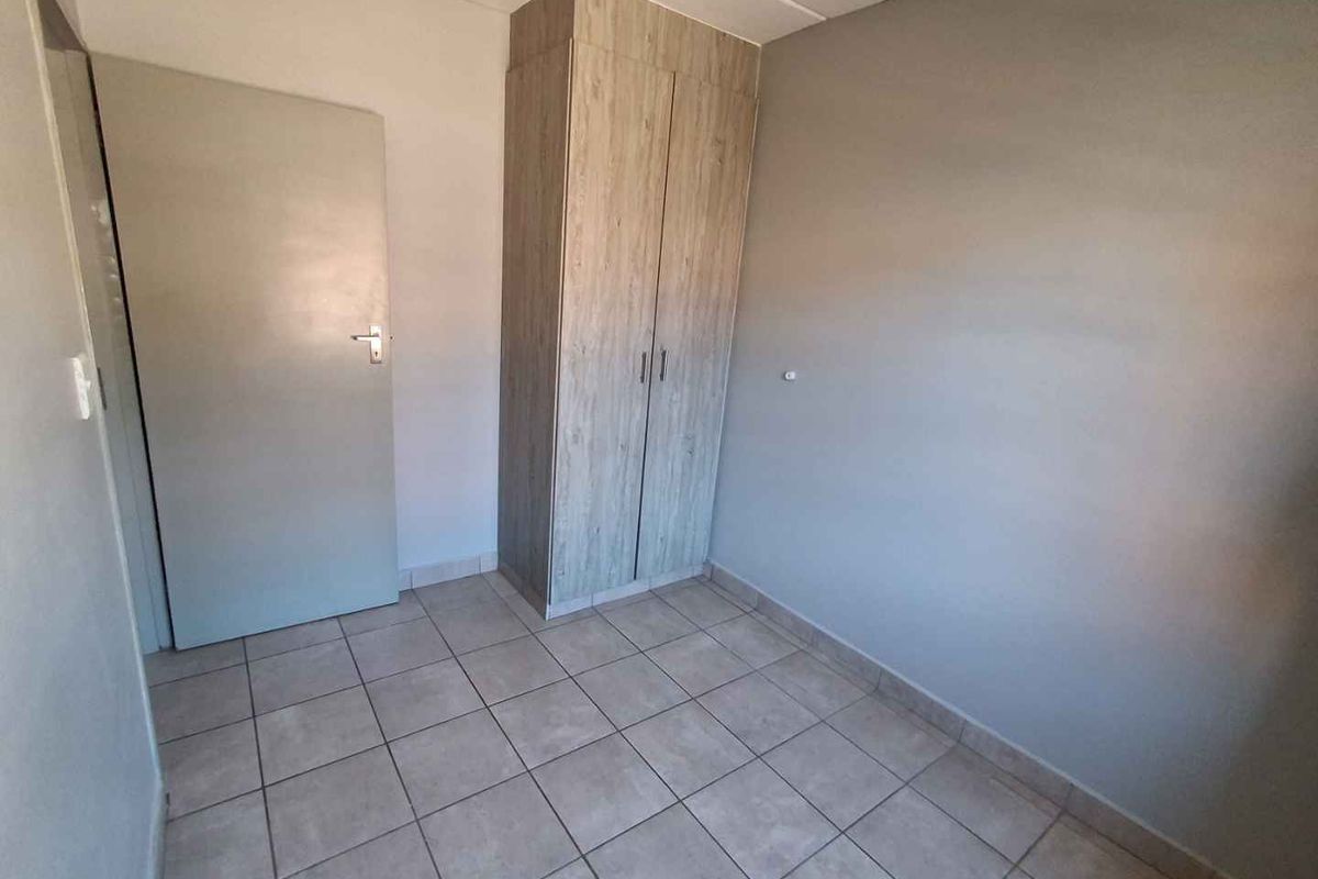 A compact bedroom featuring neutral tiled flooring and a built-in wooden wardrobe, offering a clean and functional space.