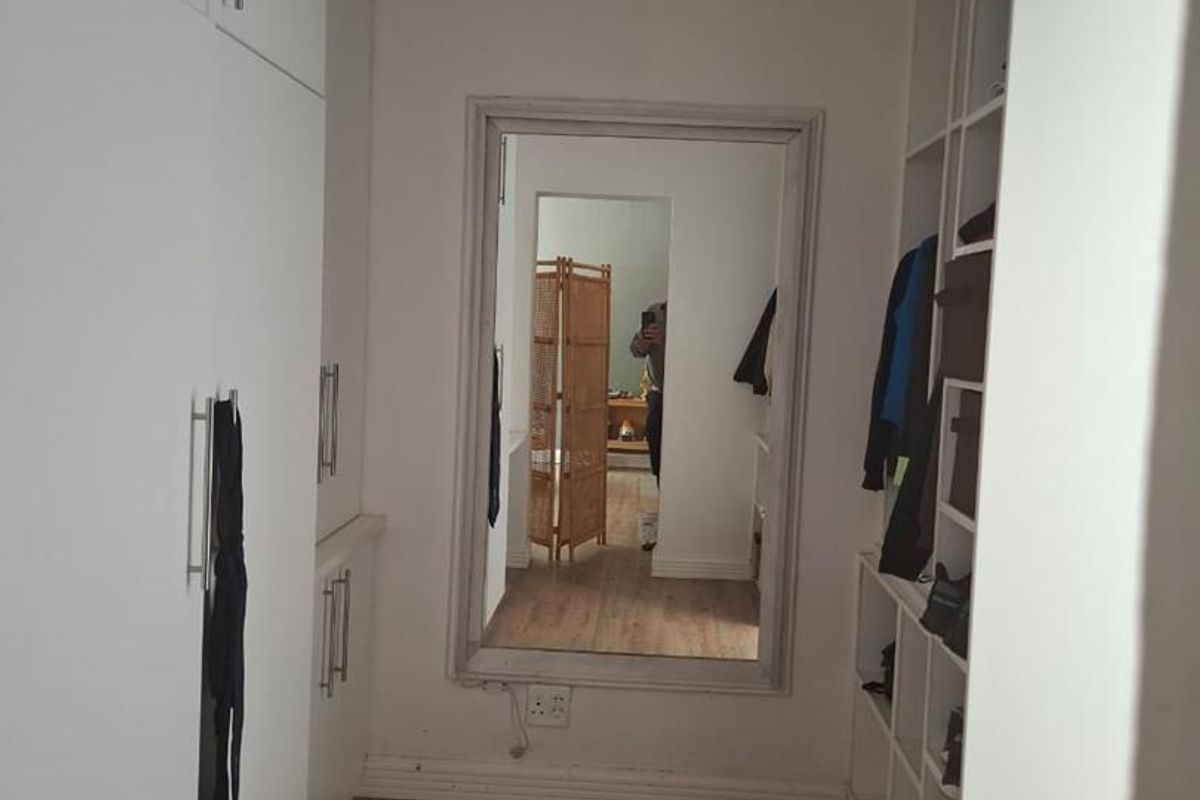 A walk-in dressing area featuring built-in white cabinetry, open shelving units, and wood-look flooring.