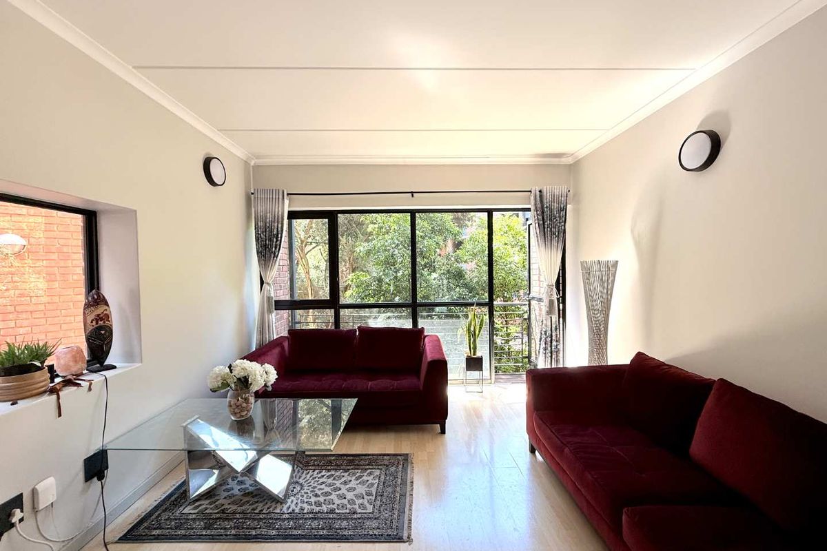 A bright and airy living room featuring large windows, light-toned flooring, and modern wall-mounted lighting fixtures.