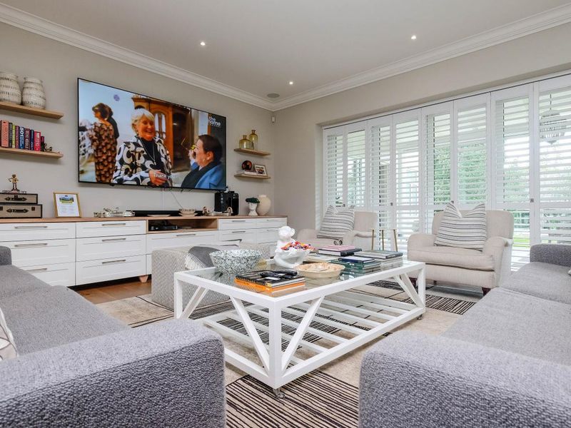 A well-appointed living room featuring custom built-in cabinetry, floating shelving, and plantation shutters, creating a bright and polished living space.