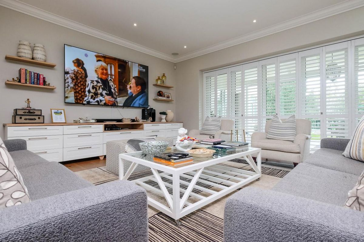 A well-appointed living room featuring custom built-in cabinetry, floating shelving, and plantation shutters, creating a bright and polished living space.