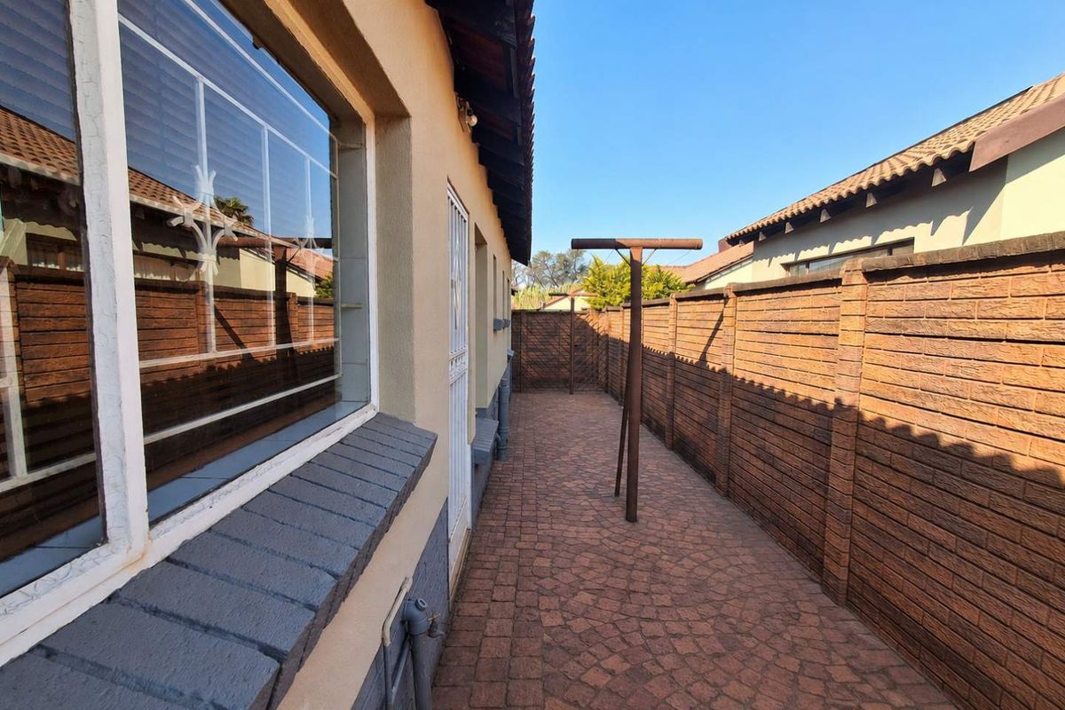 A side exterior walkway featuring paved flooring, brick boundary walls, and secure window bars along the side of the house.