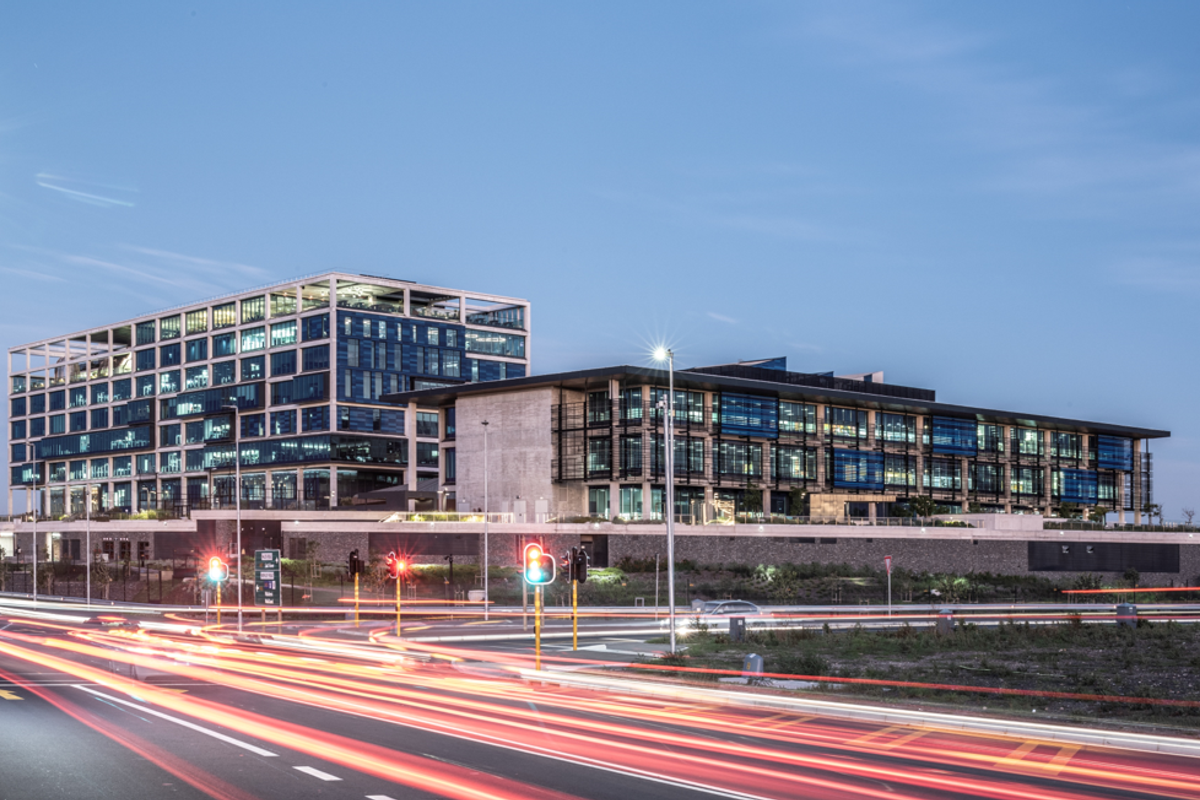 A professional evening view of a modern multi-story office complex featuring glass facades and contemporary architectural design, situated near a main road.