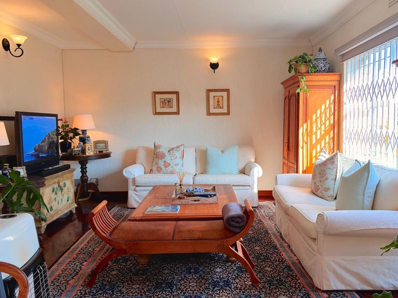 A cozy living room featuring hardwood flooring, crown molding, and wall sconce lighting, with a security gate installed on the window.