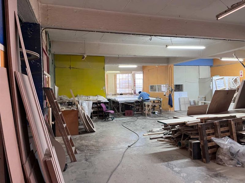 Industrial workshop space featuring exposed concrete ceilings, fluorescent lighting, and durable concrete flooring, suitable for manufacturing or storage operations.