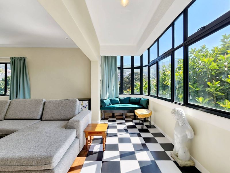A bright living area featuring large black-framed windows, checkered tile flooring, and a spacious layout with natural light.