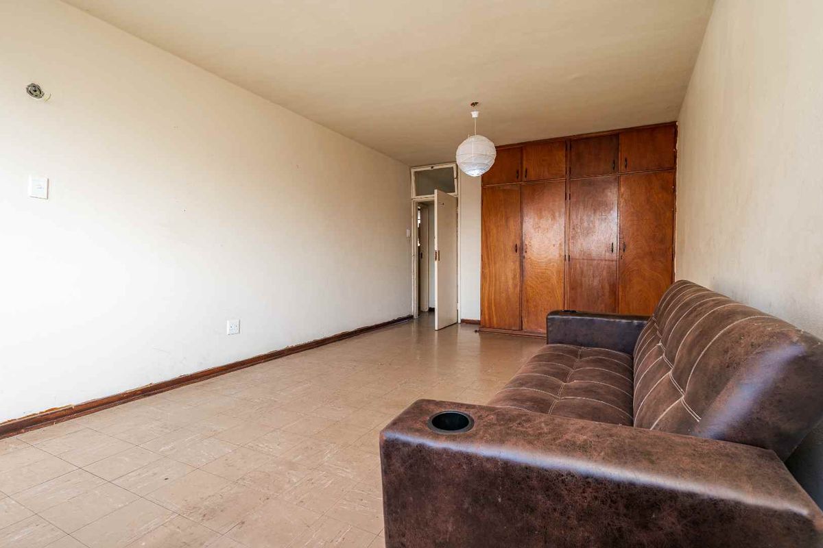 A bedroom featuring built-in wooden cupboards and tiled flooring, offering a functional space with potential for cosmetic updates to modernize the interior finishes.