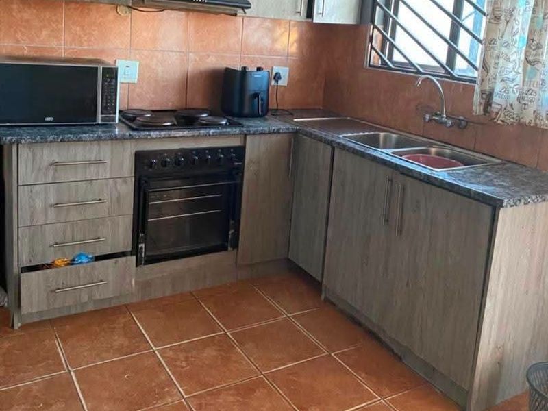 Functional kitchen featuring wood-look cabinetry, granite-style countertops, built-in oven with hob, and tiled finishes throughout.