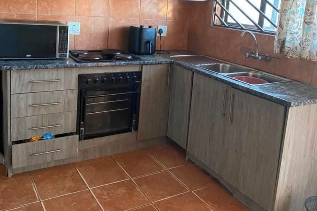 Functional kitchen featuring wood-look cabinetry, granite-style countertops, built-in oven with hob, and tiled finishes throughout.