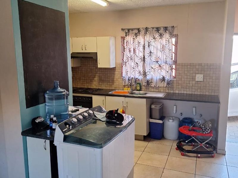 Functional kitchen area featuring built-in cabinetry, tiled backsplash, integrated hob and oven, and tiled flooring with space for laundry appliances.