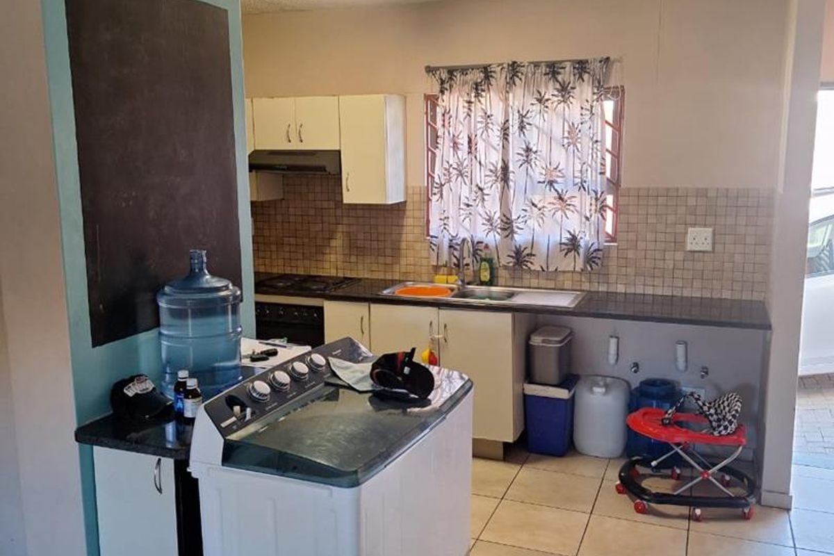 Functional kitchen area featuring built-in cabinetry, tiled backsplash, integrated hob and oven, and tiled flooring with space for laundry appliances.