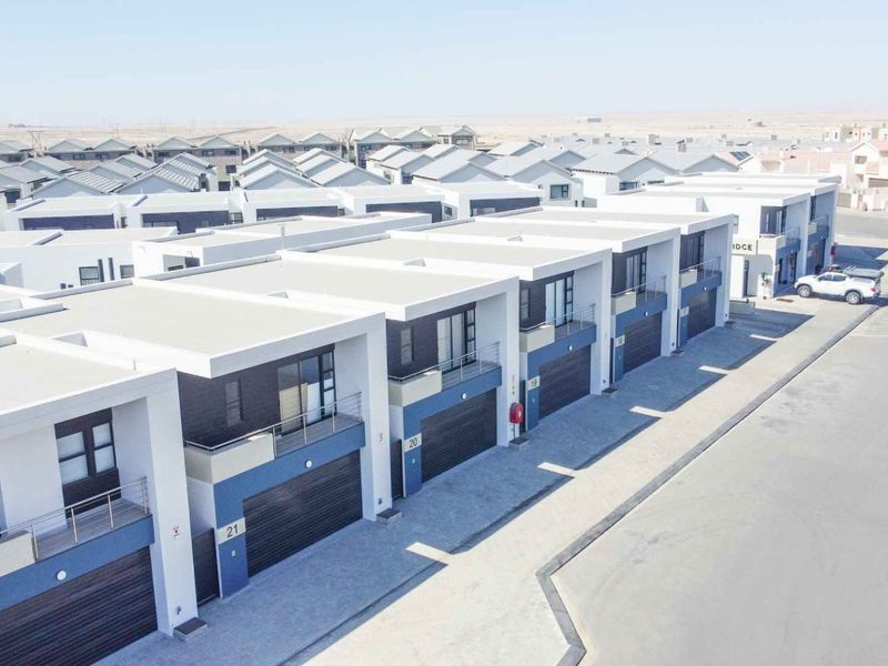 Aerial view of a modern townhouse complex featuring uniform architectural design, paved driveways, integrated garages, and private balconies.