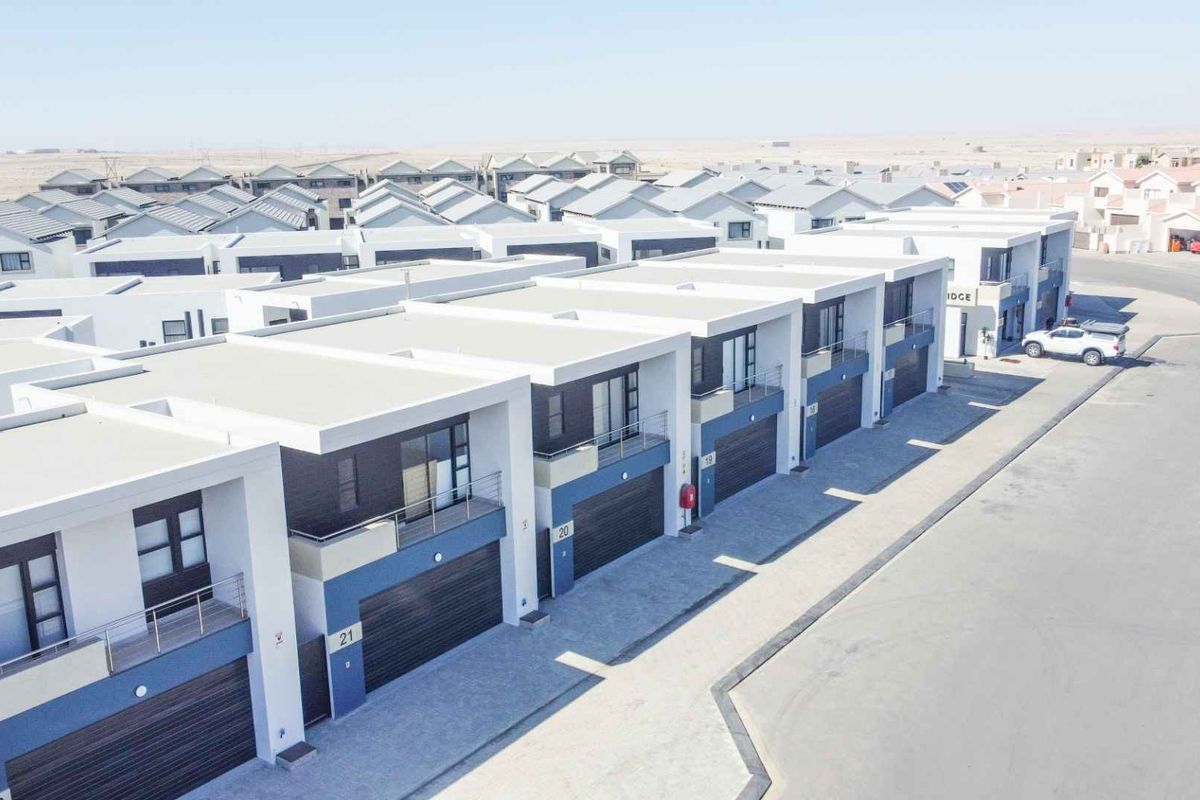 Aerial view of a modern townhouse complex featuring uniform architectural design, paved driveways, integrated garages, and private balconies.