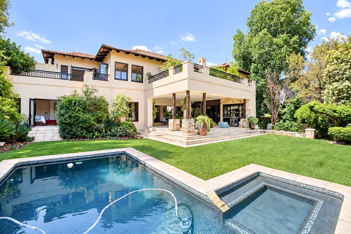 Spacious rear exterior featuring a swimming pool, integrated spa, covered patio area, and a large balcony overlooking the landscaped garden.