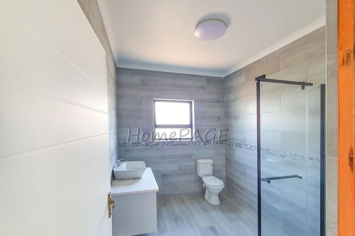 Modern bathroom featuring grey wall and floor tiles, a floating vanity with a vessel sink, a toilet, and a glass-enclosed shower.