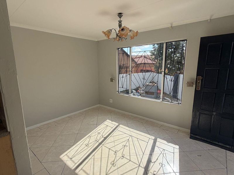 A bright, empty living area featuring tiled flooring, a security gate, and large windows with security bars, offering a clean canvas for personalization.