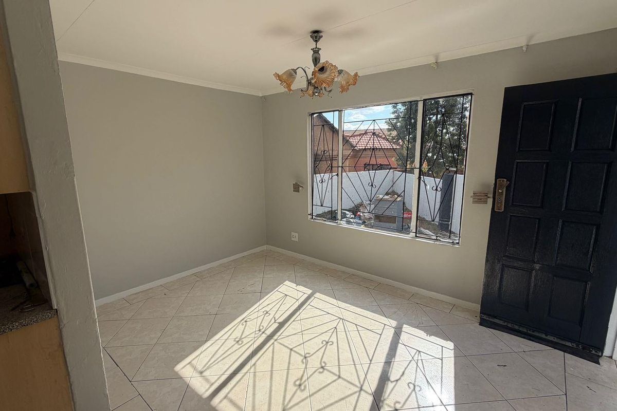 A bright, empty living area featuring tiled flooring, a security gate, and large windows with security bars, offering a clean canvas for personalization.
