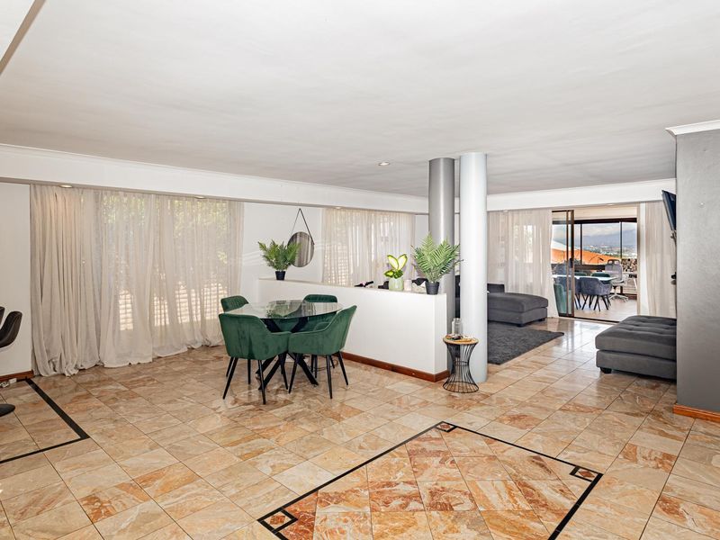 Spacious open-plan living and dining area featuring tiled flooring, structural columns, and large sliding doors leading to an outdoor patio space.