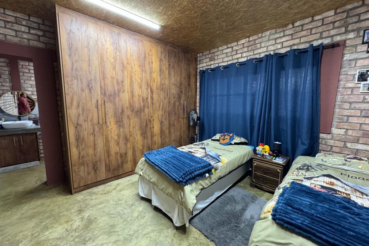 A bedroom featuring exposed brick walls, a wood-paneled ceiling, polished concrete flooring, and extensive built-in wooden cabinetry, with an adjoining en-suite bathroom area.